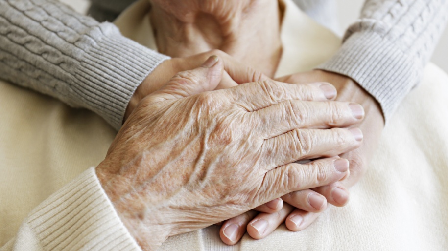 Elderly hands clasped together showing vulnerability and need for care